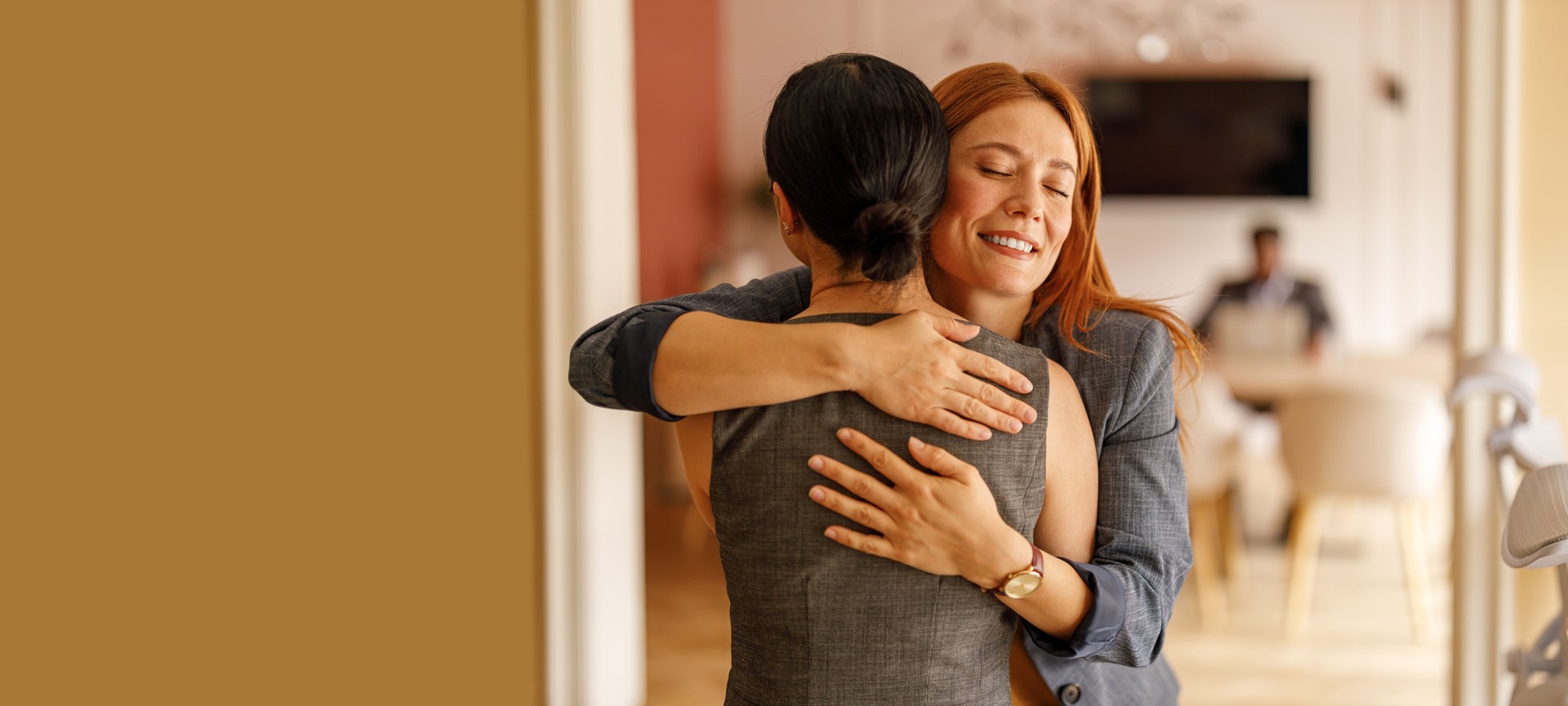 Smiling businesswoman with eyes closed embracing female colleague and welcoming her in office meeting